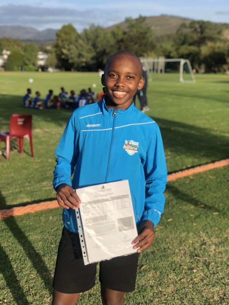 A player of the Young Bafana Soccer Academy standing on a soccer pitch in South Africa with a certificate in his hands.