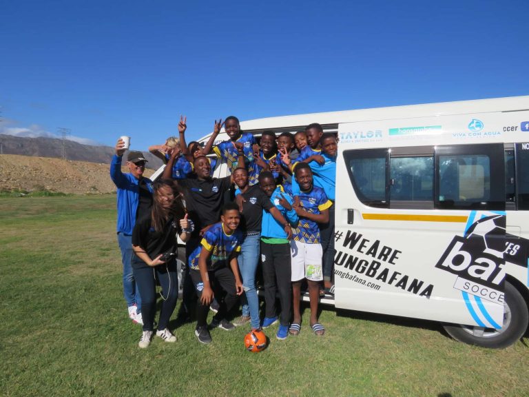 Members of the NGO Young Bafana Soccer Academy celebrating in a bus on a soccer field during the YB Arena opening.