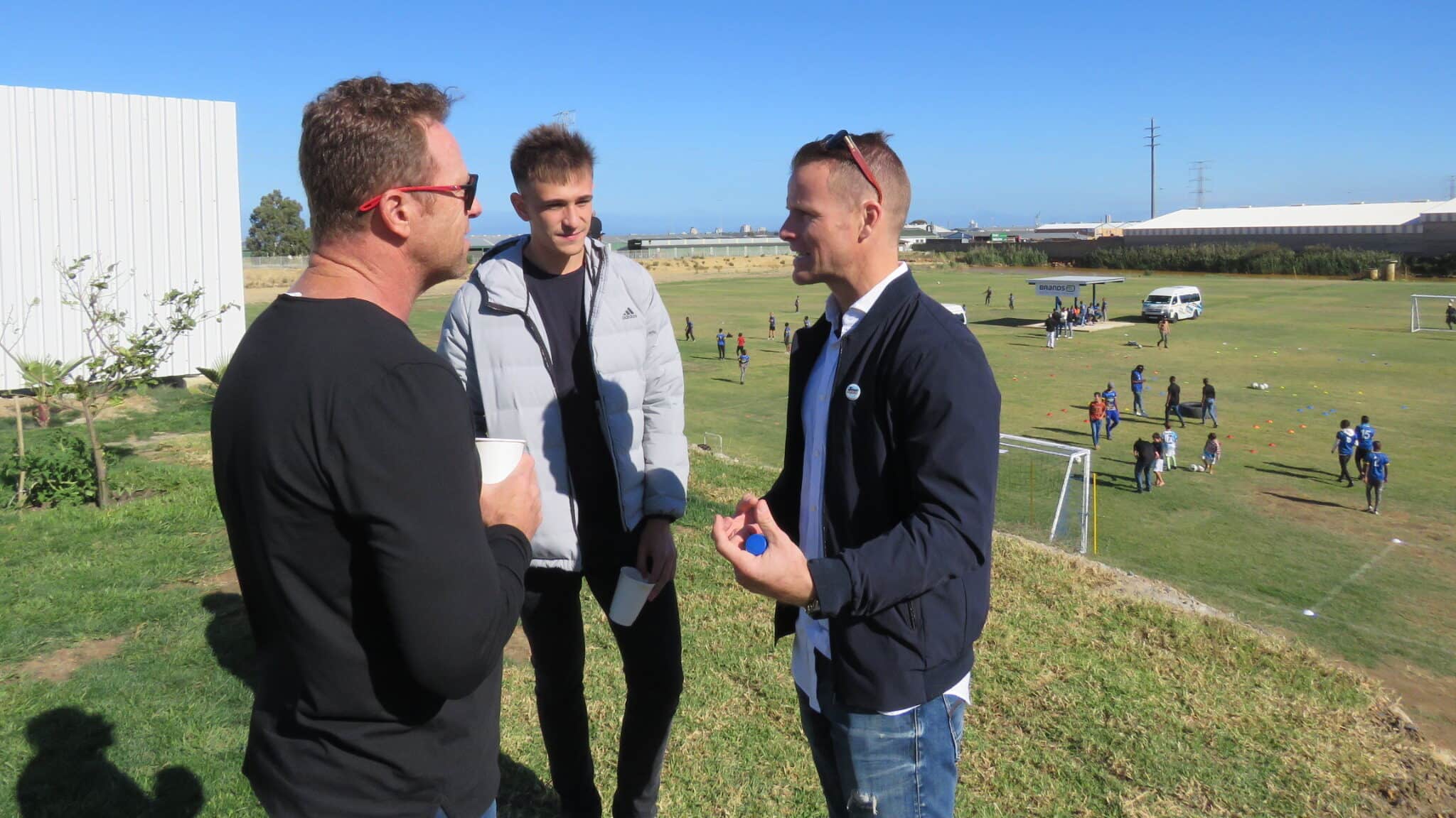 Three men having a chat in front of a soccer pitch during the YB Arena opening.