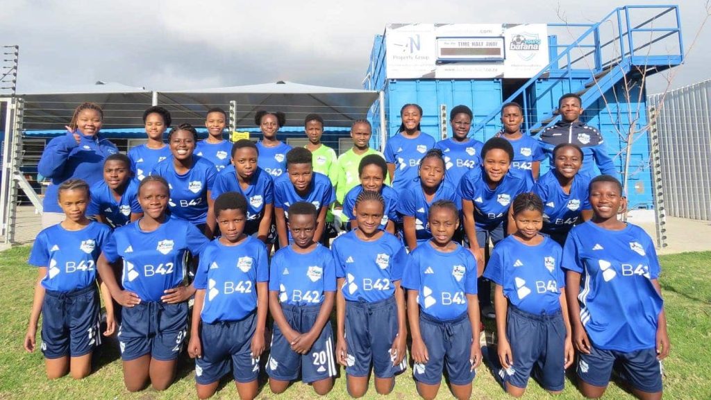 Team photo of the Young Bafana Soccer Academy girls team in front of the YB Arena.